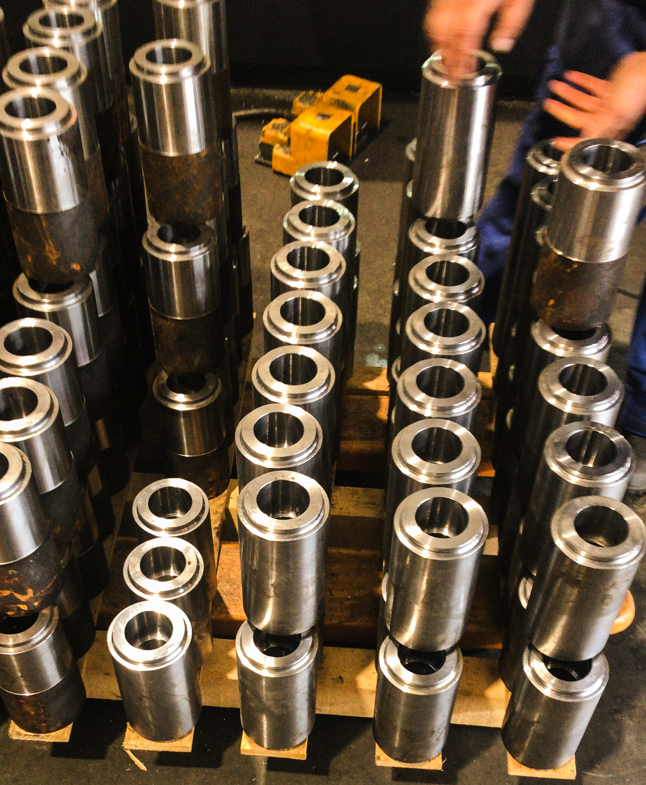 Bewerker stapelt glanzende metalen cilinders met holle kern op houten blokken in een werkplaats, met roestige en schone onderdelen door elkaar.