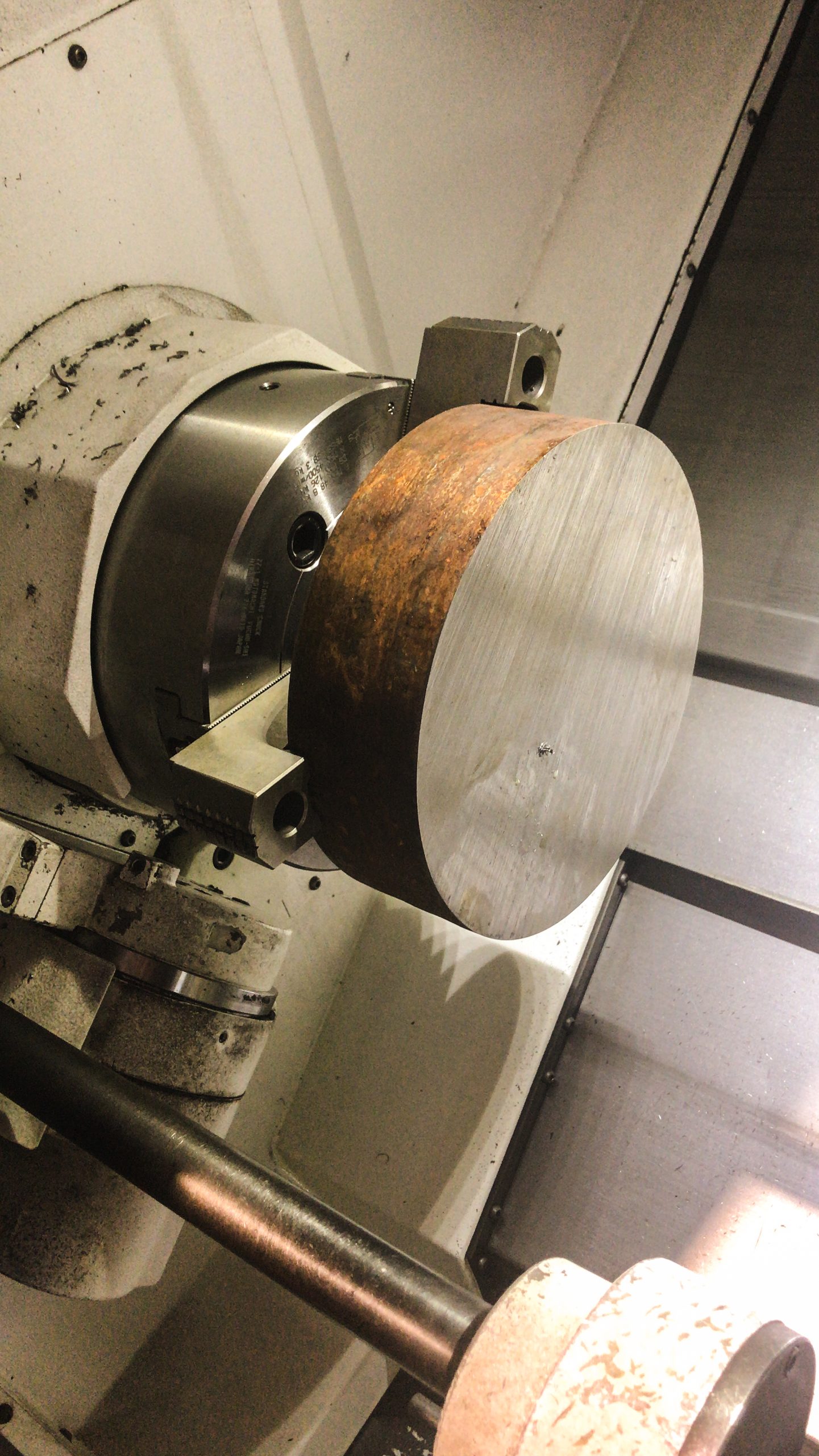 Groot cilindervormig metalen werkstuk, deels geroest, vastgeklemd in een draaibank voor bewerking in een werkplaats