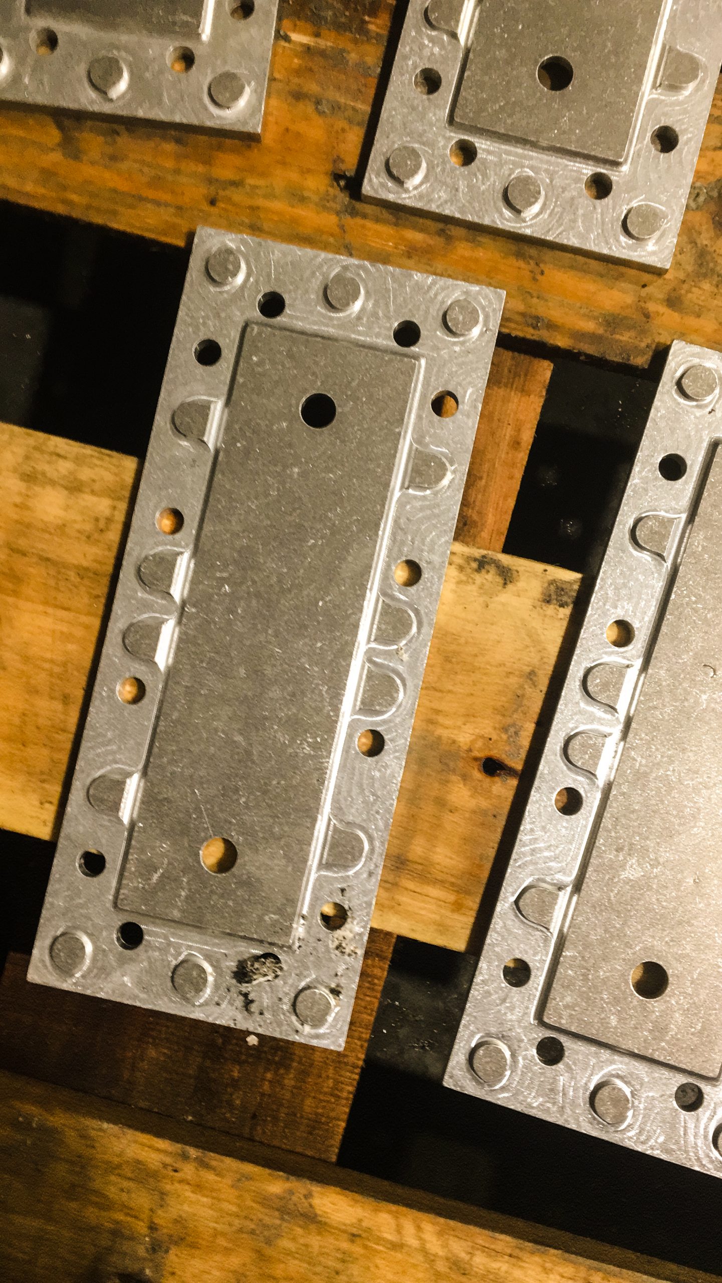 Bewerkt metalen bevestigingsplaten met gatenpatroon, netjes gerangschikt op een houten pallet in een werkplaats.