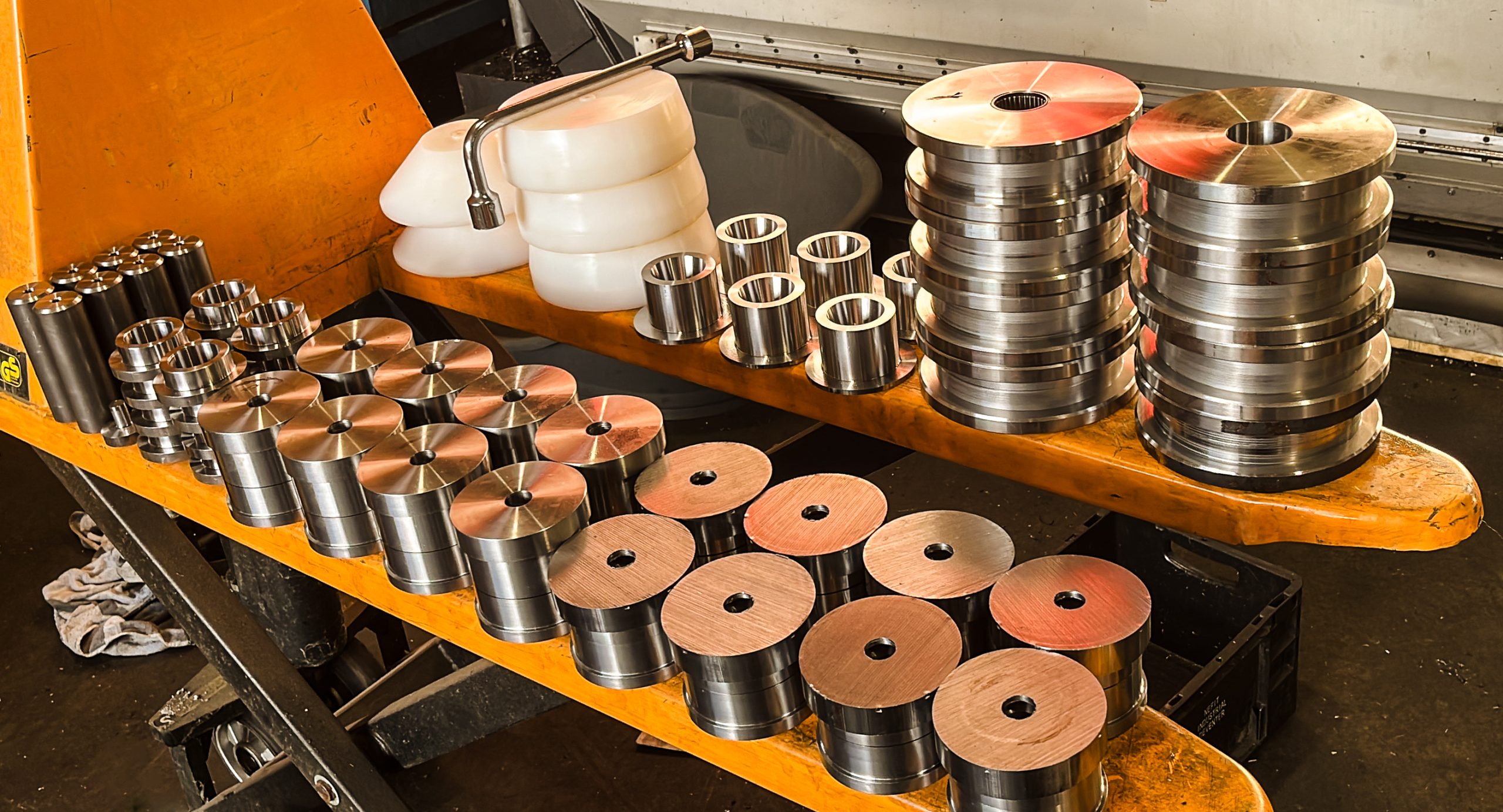 Verschillende bewerkte metalen en kunststof onderdelen, netjes gerangschikt op een gele werktafel in een werkplaats.