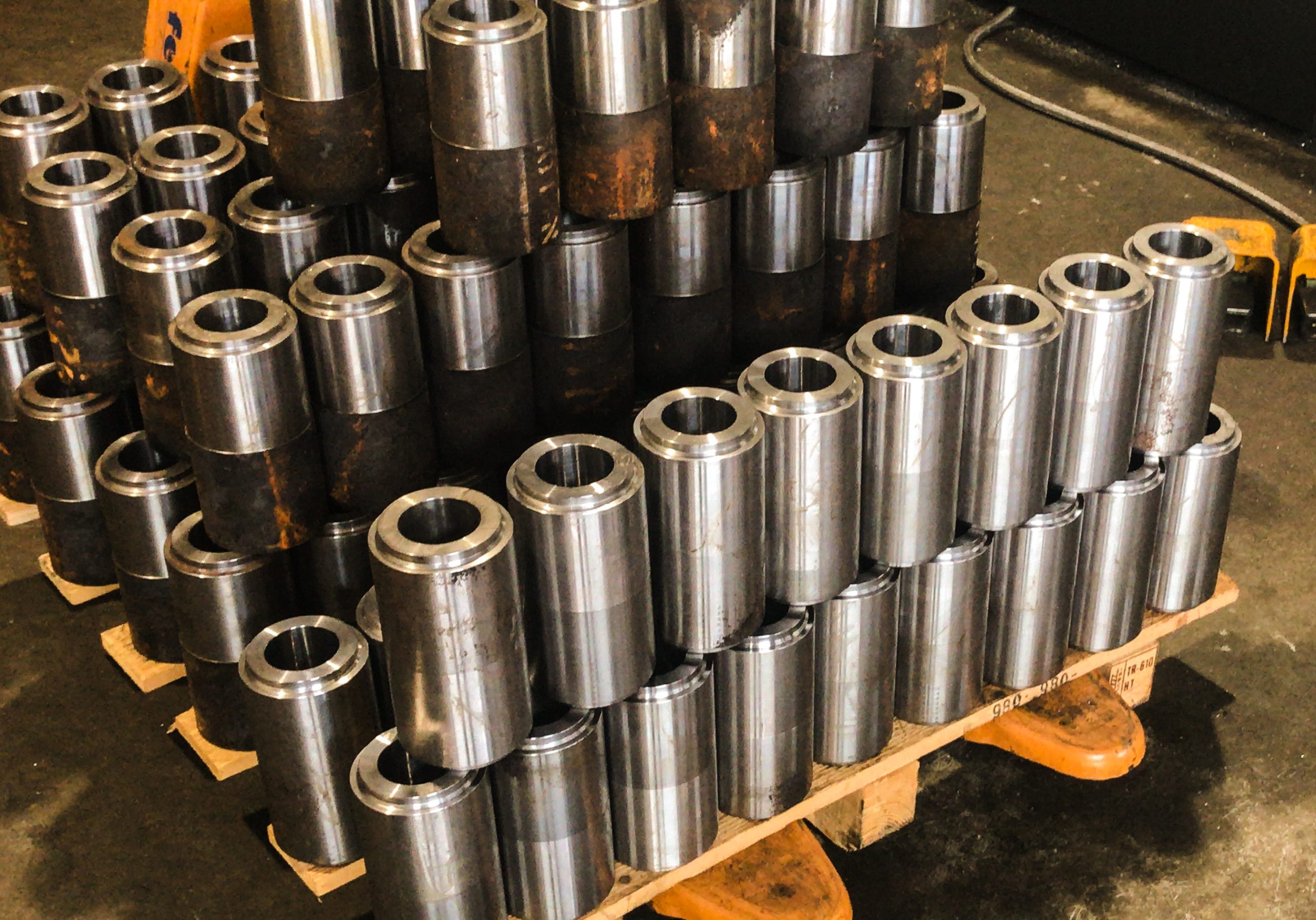 Stapel bewerkte metalen cilinders met een glanzend en roestig oppervlak, netjes gerangschikt op een houten pallet in een werkplaats.