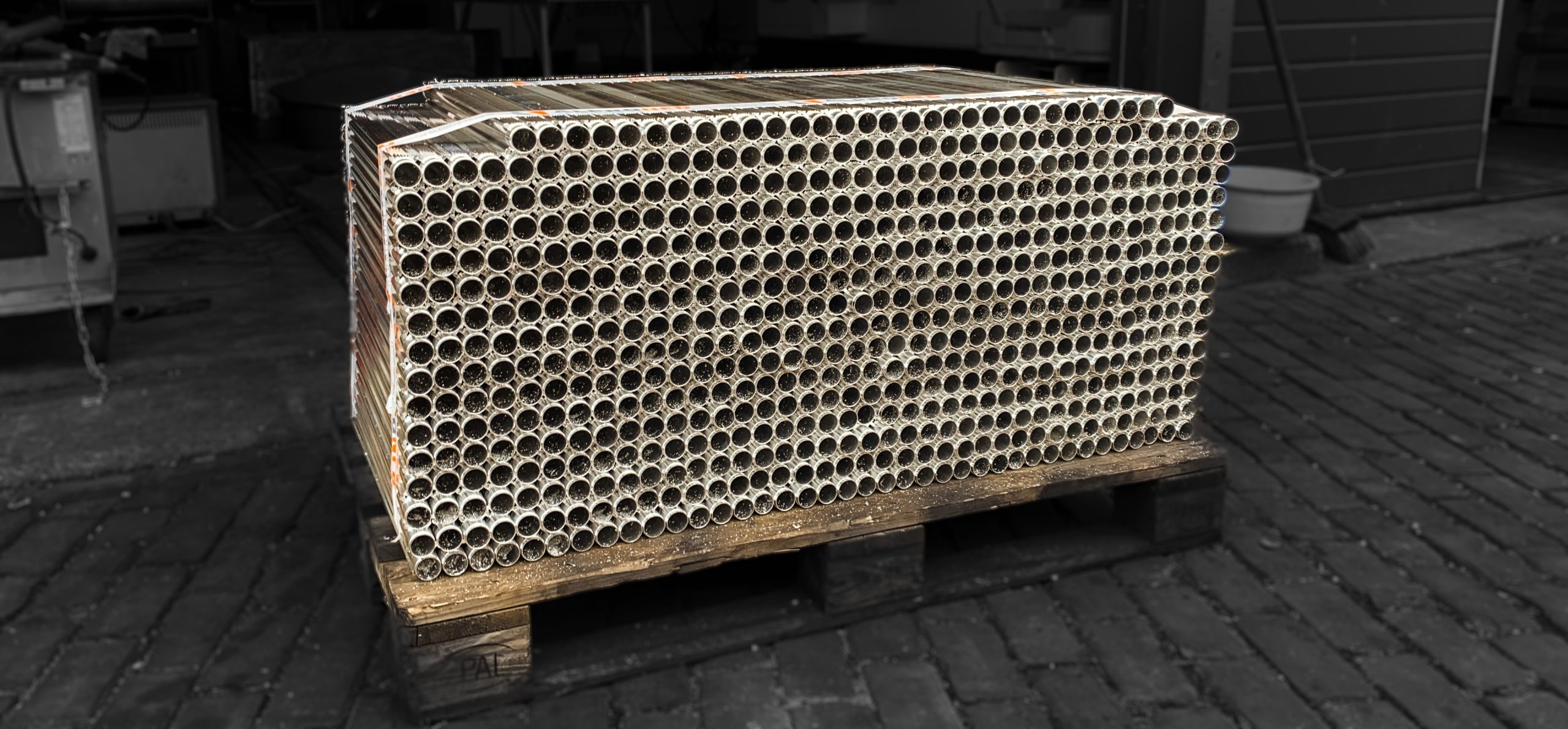 Grote stapel aluminium buizen netjes gebundeld en geplaatst op een houten pallet in een werkplaatsomgeving.