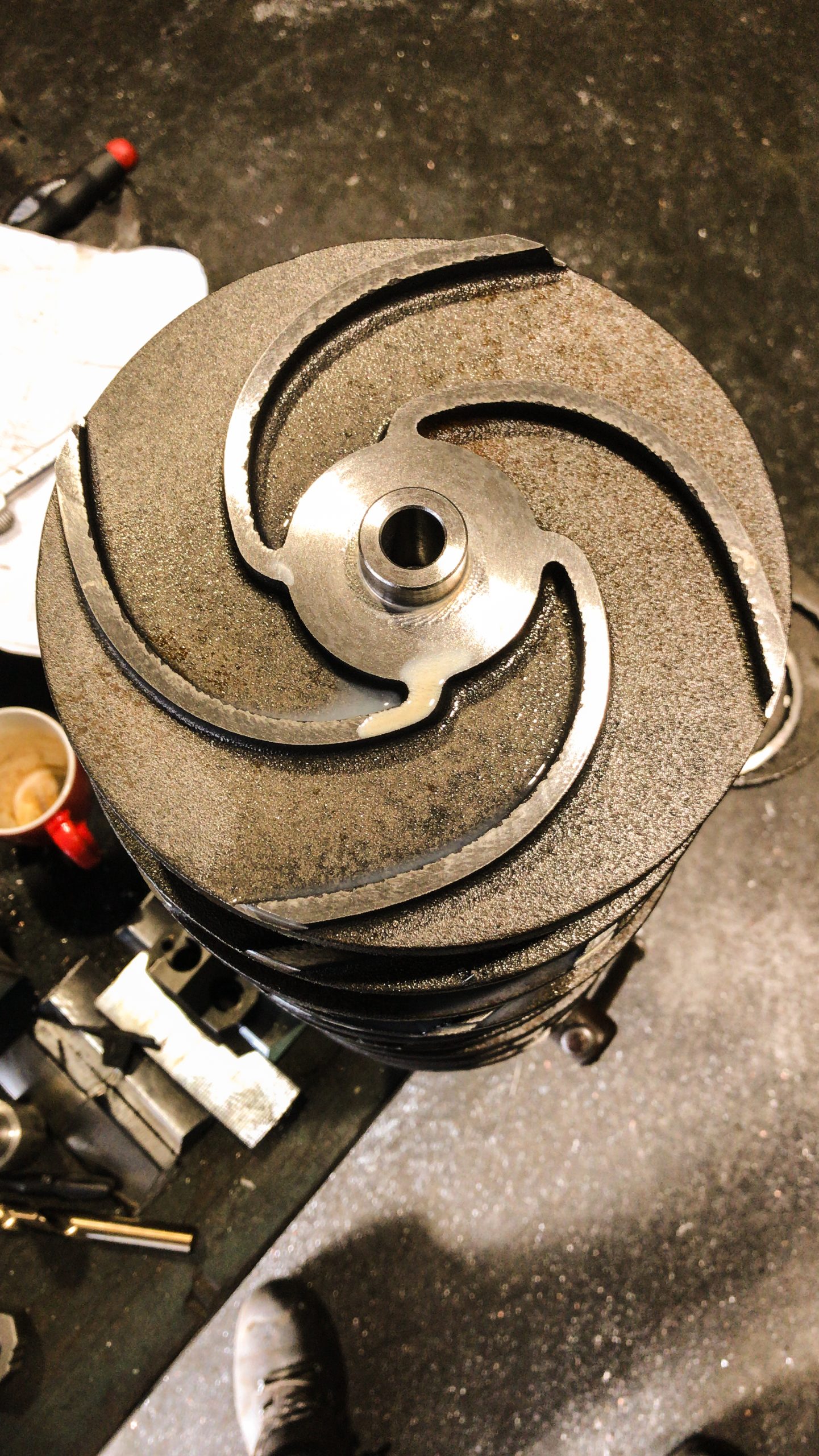 Metalen pompwaaier met zichtbare slijtage en opgeruwd oppervlak, liggend op een werkbank in een werkplaats.