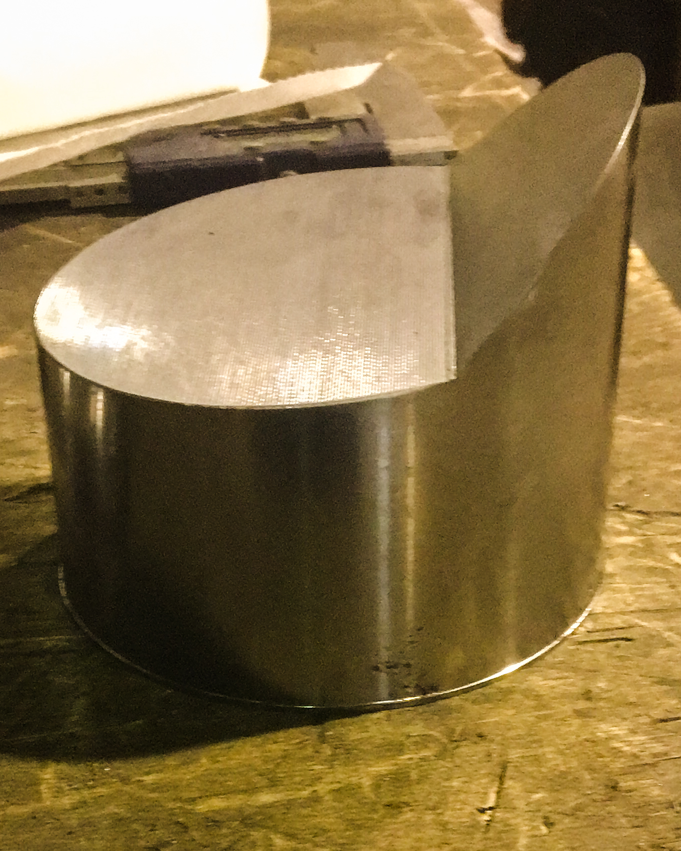 Bewerkt halfrond metalen werkstuk met een gladde afwerking, liggend op een houten werkbank met gereedschap op de achtergrond.