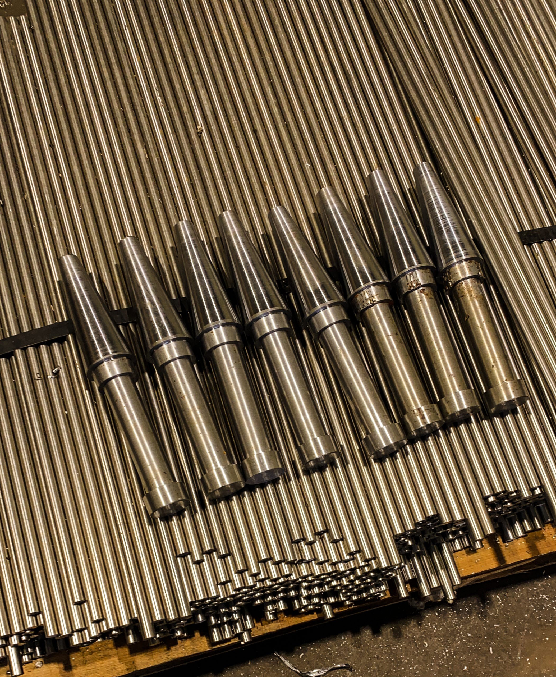 Stapel nauwkeurig bewerkte metalen staven en conische assen op een houten ondergrond in een werkplaats.