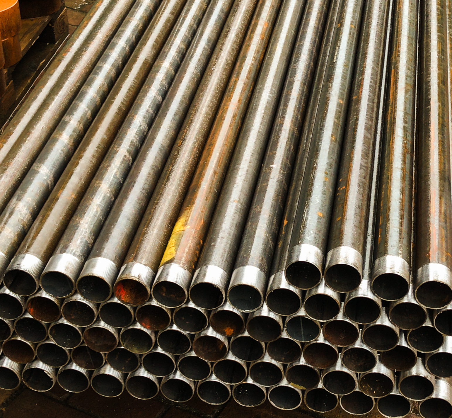 Een stapel metalen buizen met schroefdraad aan de uiteinden, geschikt voor constructie en industriële toepassingen.